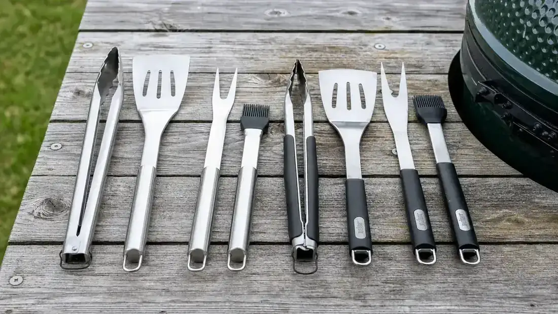 Backyard grill setup with BBQ tools laid out on a wooden side table next to a charcoal grill