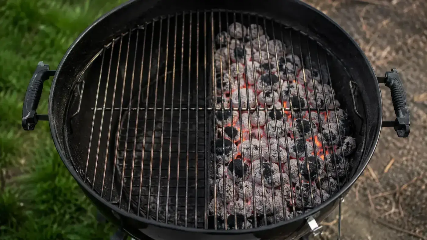 Weber Original Kettle charcoal grill with lid off showing two distinct zones of charcoal and empty cooking grate at dusk in a backyard