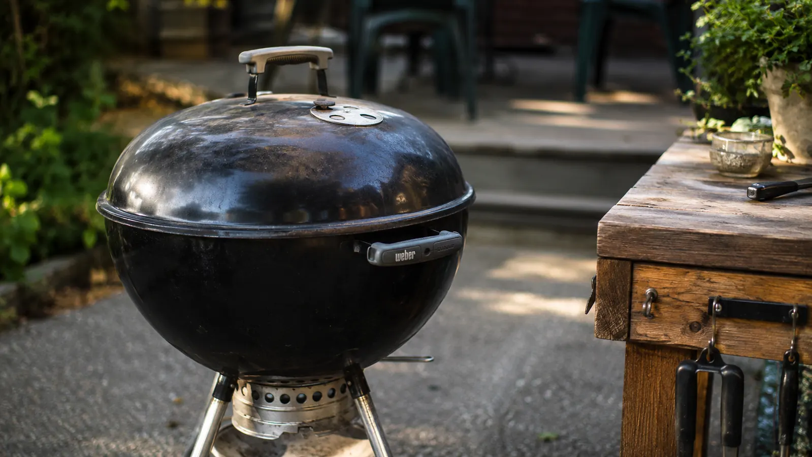 Weber Original Kettle 22-inch charcoal grill on a backyard patio in morning light with smoke rising from the lid