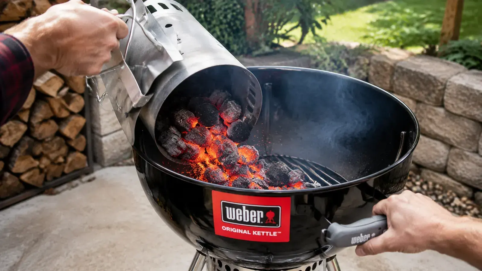 Hand placing a chimney starter full of lit coals into a Weber kettle grill grate