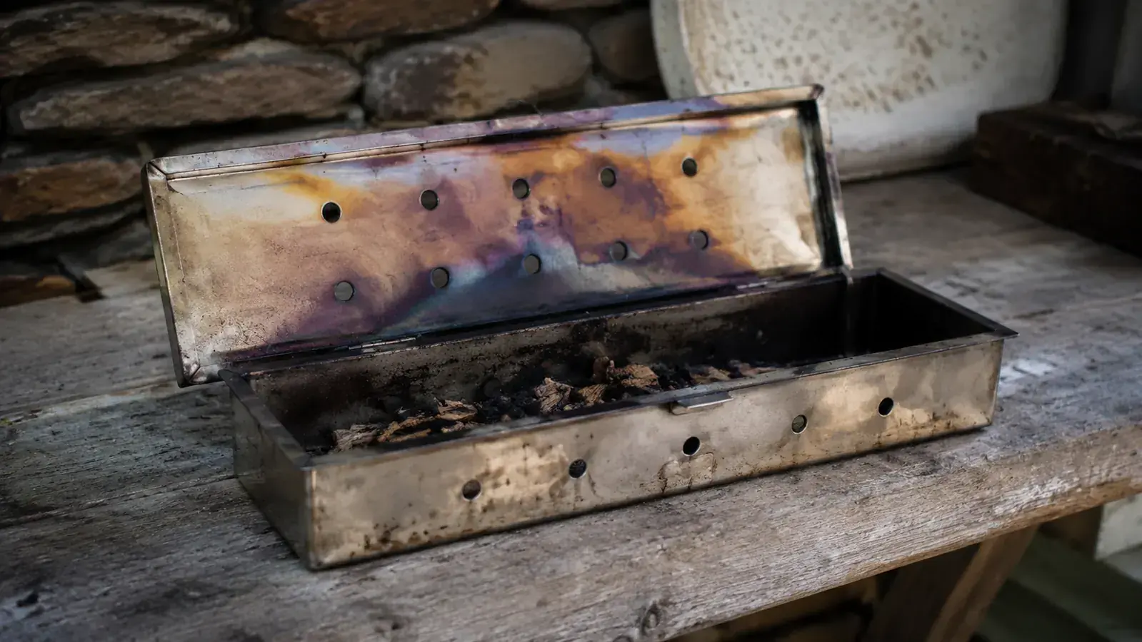 Weber Premium Smoker Box sitting on a gas grill grate with thin blue smoke rising, backyard setting at dusk